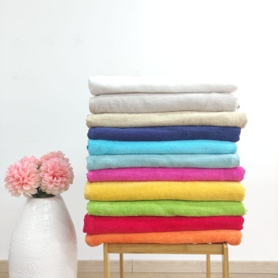 Pilhas de toalhas coloridas empilhadas em madeira ao lado de um vaso branco com flores cor-de-rosa