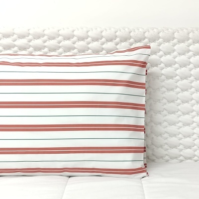 Travesseiro com fronha riscada em castanho e verde sobre colchão branco acolchoado