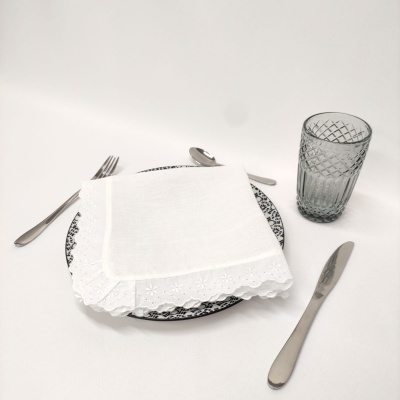 Mesa posta com talheres de aço inoxidável, prato branco com padrão preto, guardanapo branco bordado e copo de vidro transparente