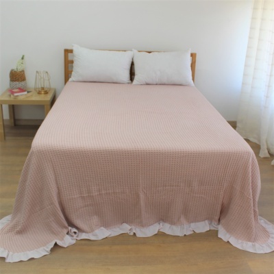 Cama de casal com colcha rosa texturizada e almofadas brancas