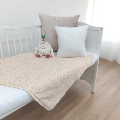 Berço branco com colcha creme floral, almofadas branca e rosa, e pelúcia de alho