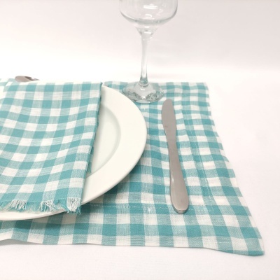 Guardanapo e toalha de mesa quadriculados em azul turquesa e branco, prato branco, faca de metal e copo de vidro