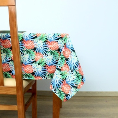 Toalha de mesa com padrão de abacaxis e folhas em cores vivas sobre mesa de madeira