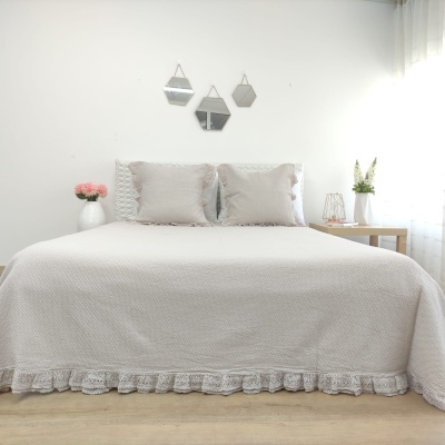 Cama com colcha branca e almofadas cinzentas em quarto minimalista com mesas laterais e vasos de flores