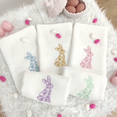 Toalhas brancas com bordados de coelhos coloridos e ovos decorativos ao redor