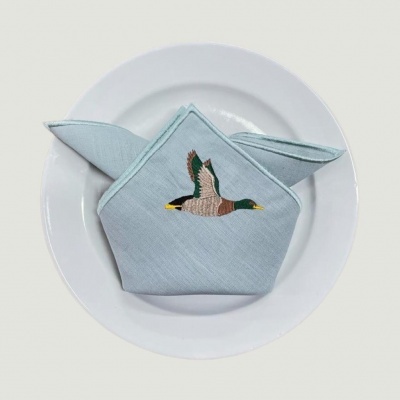 Guardanapo azul claro com bordado de pato dentro de prato branco redondo