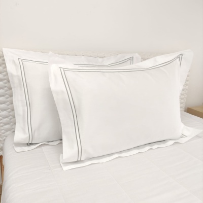 Almofadas brancas com riscas cinzentas e moldura dupla em cama branca