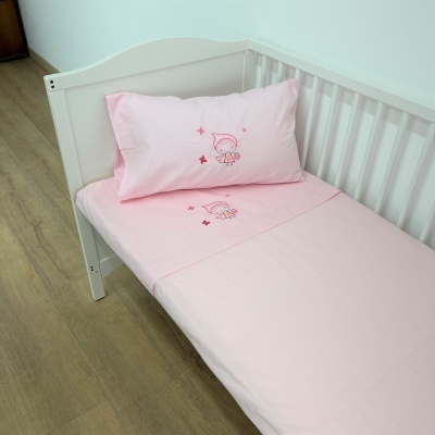 Lençóis rosa claro com estampa de boneco e almofada com o mesmo padrão numa cama de madeira branca