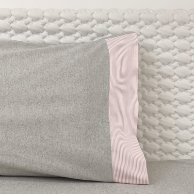 Fronha cinzenta com aba rosa às riscas sobre almofada branca texturada