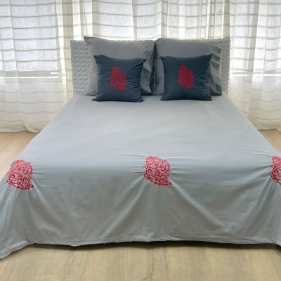 Cama com roupa de cama cinza e almofadas com bordados vermelhos