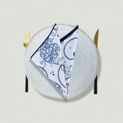 Prato cinza claro com guardanapo branco e azul e talheres dourados sobre fundo cinza