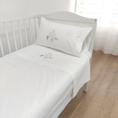 Cama infantil branca com roupa de cama branca decorada com bordado de urso e texto