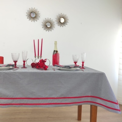 Mesa decorada com toalha xadrez preta e branca com borda vermelha, velas e taças vermelhas, fundo com espelhos decorativos