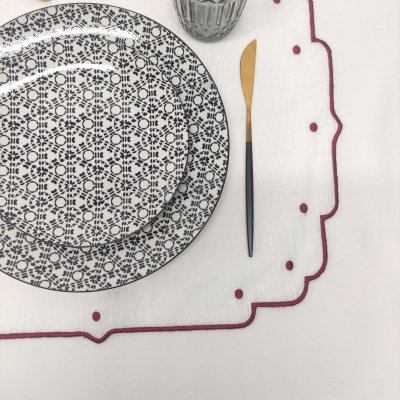 Pratos cerâmicos com padrão floral, faca metálica dourada e preta, copo de vidro e toalha branca bordada