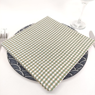 Guardanapo quadriculado verde e branco sobre prato azul e branco com talheres e copo