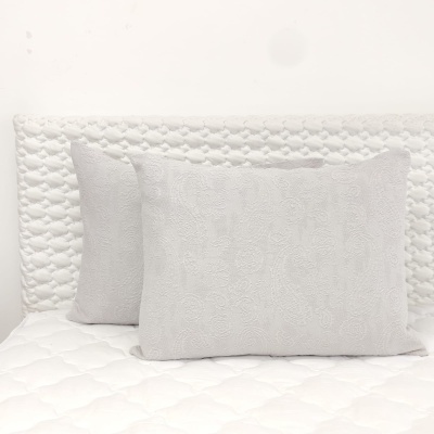 Duas almofadas brancas bordadas em relevo sobre colchão branco com cabeceira texturizada