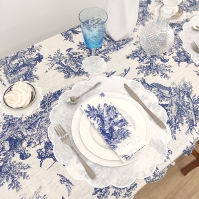 Mesa de jantar com toalha azul e branca, pratos brancos, talheres e copo azul
