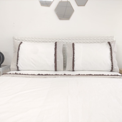 Cama com fronhas e cabeceira brancas com padrão cinza e castanho, três espelhos hexagonais na parede