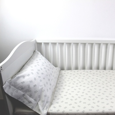 Berço branco com colchão e almofada com roupa de cama branca com desenhos cinzentos