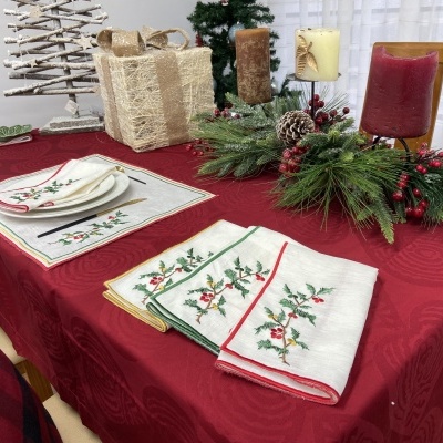 Mesa de Natal decorada com toalha vermelha, guardanapos bordados, velas e arranjo com pinheiro