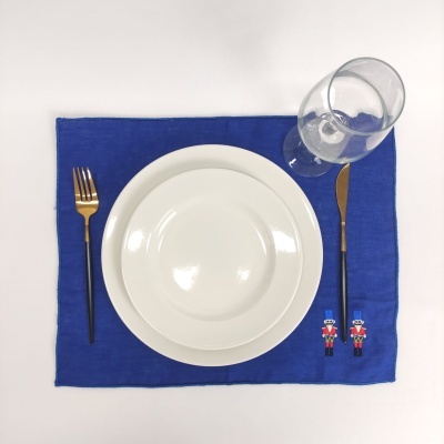 Conjunto de jantar com guardanapo azul, prato branco, talheres preto e dourado e copo de vidro