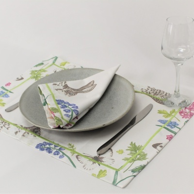 Mesa posta com guardanapo e círculo individual floral, prato cinza, talheres e copo de vidro