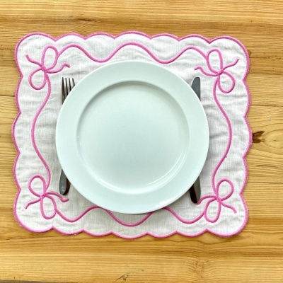 Pegador de mesa branco com bordados cor-de-rosa e prato branco num suporte de madeira