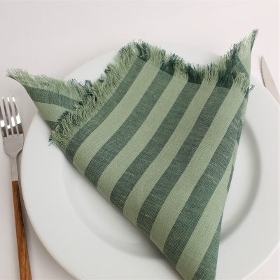 Guardanapo listrado verde com franjas sobre prato branco, garfo e faca ao lado.