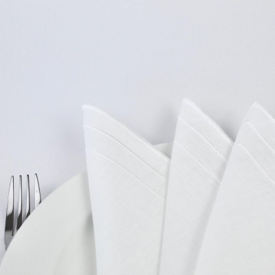 Guardanapos de tecido brancos dobrados sobre prato branco com garfo metálico ao lado