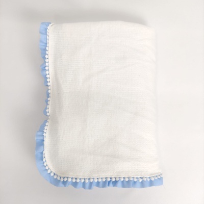 Manta branca com borda azul e pompons brancos