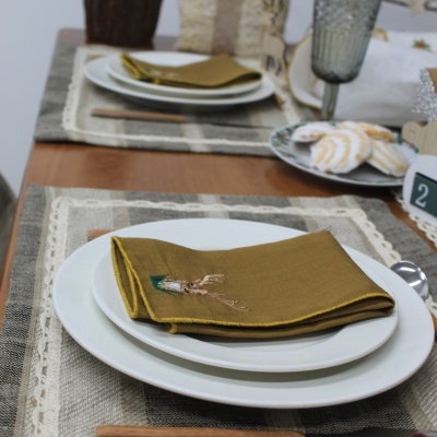 Mesa posta com pratos brancos, guardanapos castanhos, talheres de madeira e copo cinza escuro