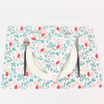 Jogo americano e guardanapo com padrão floral colorido, prato branco e talheres sobre superfície branca