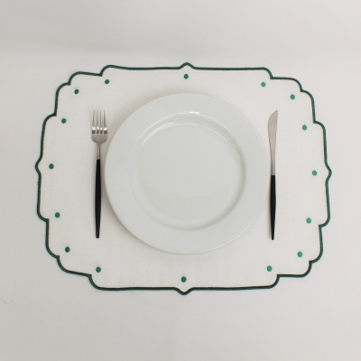 Mesa posta com prato branco, individual branco com borda verde, garfo e faca com cabo preto