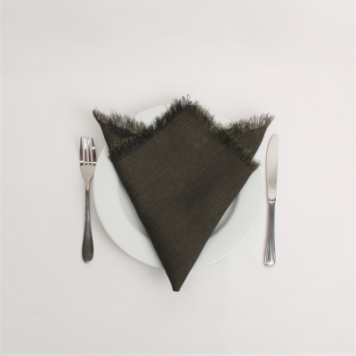 Guardanapo castanho escuro com franjas sobre prato branco, garfo e faca ao lado