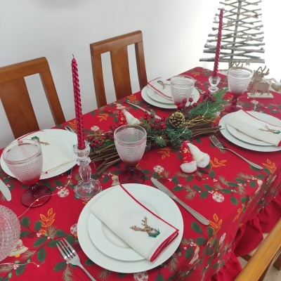 Mesa de jantar decorada para Natal com toalha vermelha, pratos brancos, guardanapos com rena e velas vermelhas.