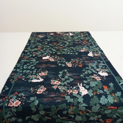 Toalha ou tecido decorativo com padrão de folhas, flores e coelhos