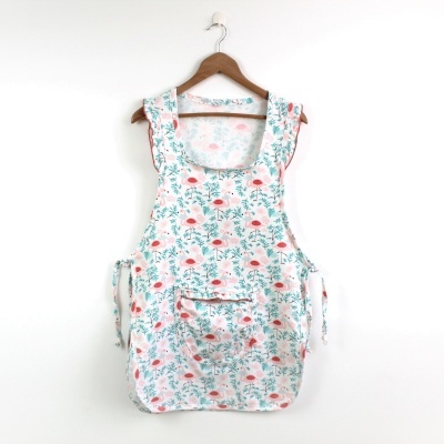 Avental branco com padrão floral vermelho e verde pendurado num cabide