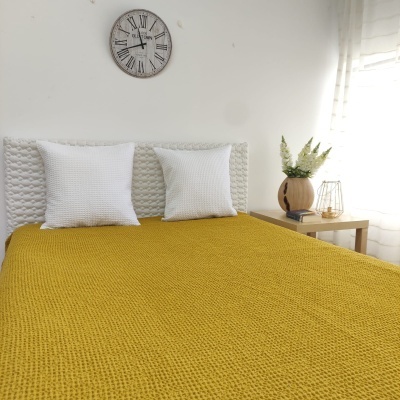 Cama com colcha amarela e duas almofadas brancas perto de mesa de cabeceira com vaso e flores