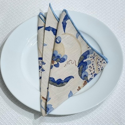 Guardanapo de tecido dobrado com padrão floral azul e bege sobre um prato branco