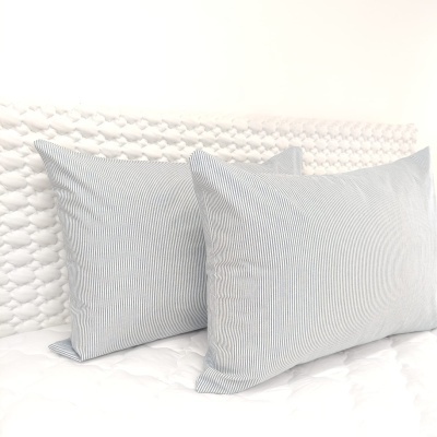 duas fronhas de almofadas riscas cinza e branco sobre cama branca com cabeceira acolchoada branca