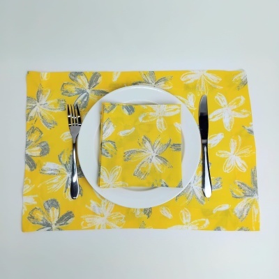 Conjunto de prato branco com guardanapo e toalha de mesa amarelos com flores e talheres metálicos