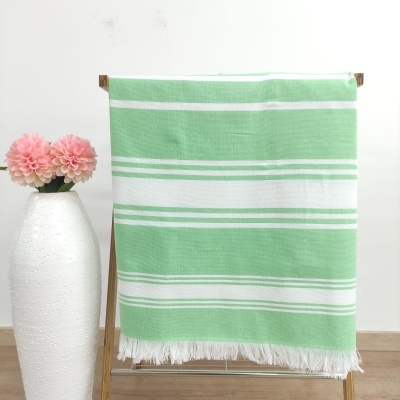 Toalha verde clara com riscas brancas pendurada numa estrutura de madeira ao lado de um vaso branco com flores cor-de-rosa