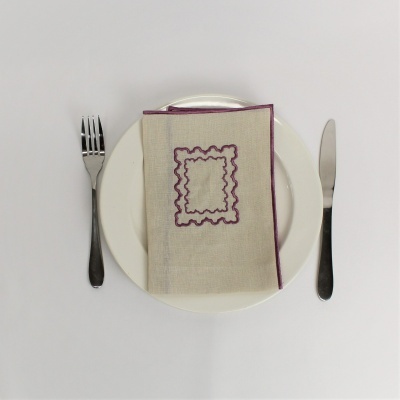 Conjunto de jantar com prato, guardanapo bordado roxo, garfo e faca sobre superfície branca