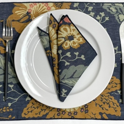 Conjunto de mesa com toalhete e guardanapo floral azul e amarelo, prato branco e talheres prateados.