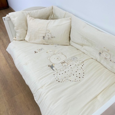 Cama branca com roupa de cama bege e padrão bordado de urso