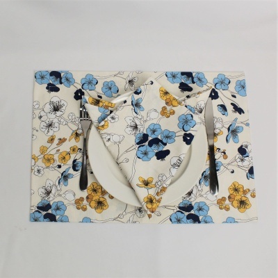 Conjunto de prato branco com guardanapo e descanso de prato florais azuis e amarelos e talheres metálicos