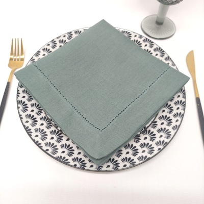 Mesa posta com prato padrão negro em porcelana, guardanapo verde, talheres dourados e copo fosco cinza.