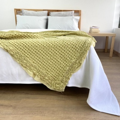 Cama com manta amarela e almofadas cinza em quarto com mesa de cabeceira e livros