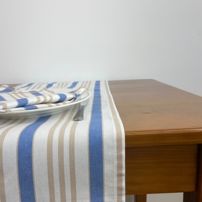 Caminho de mesa riscado azul, bege e branco numa mesa de madeira com pratos e guardanapo