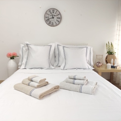 Cama branca arrumada com toalhas bege e cinza dobradas no centro